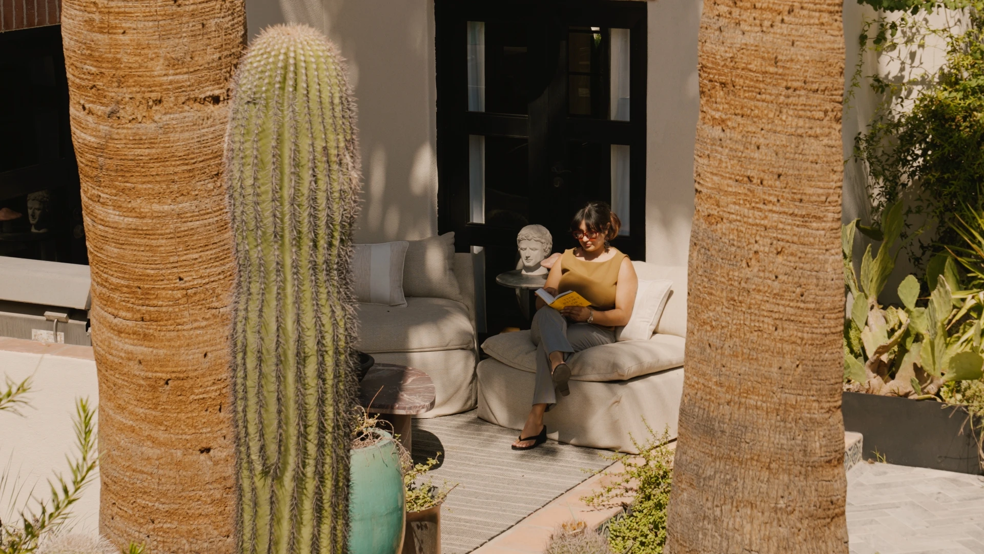 Woman reading on a patio between a saguaro and palm trunks